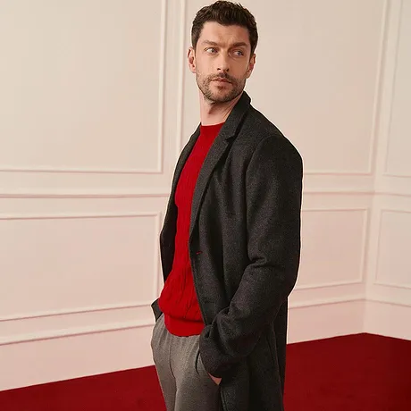 Elegante cappotto grigio sopra un maglione rosso, abbinato a pantaloni grigi coordinati.