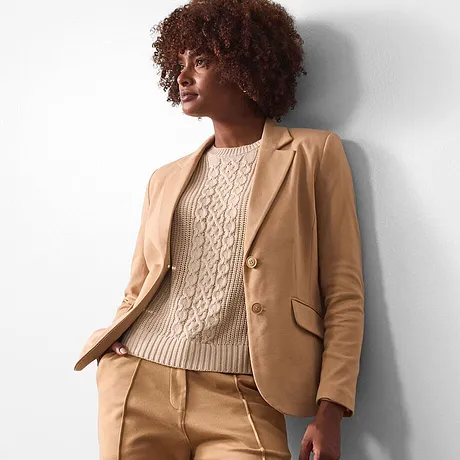 Blazer beige abbinato a un maglione lavorato a maglia color crema.