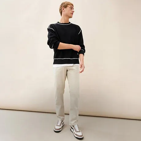 Look casual con maglione nero, pantaloni chiari e sneakers sportive.