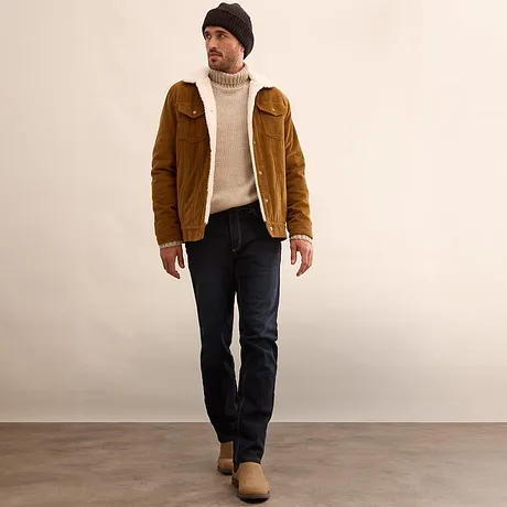 Giacca marrone, maglione a collo alto color crema e jeans scuri.