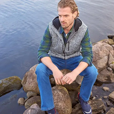 Un gilet fantasia sopra una camicia verde, abbinato a jeans blu.