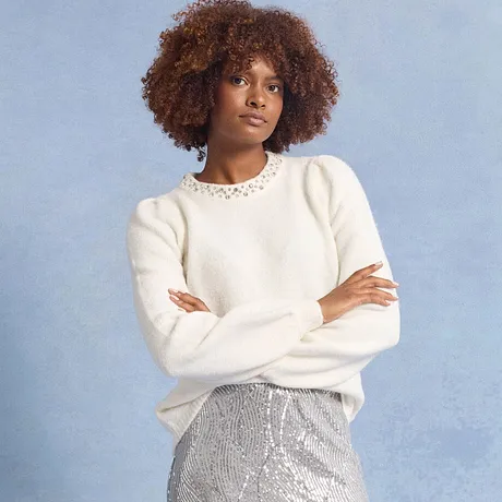 Maglione bianco con collo in pizzo, abbinato a una gonna argentata scintillante.