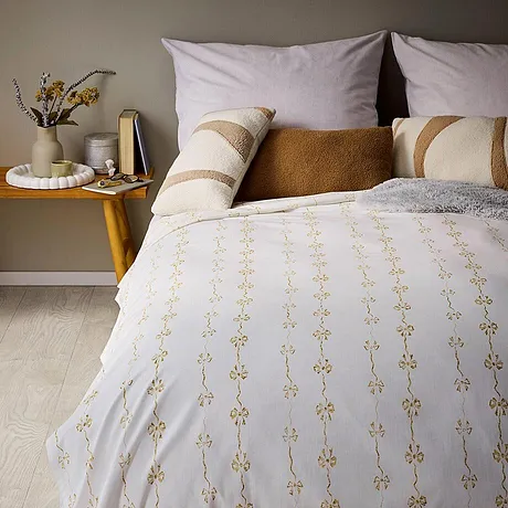 Biancheria da letto bianca, motivi beige e dorati e diversi cuscini decorativi.