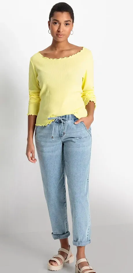 Outfit estivo: maglione giallo con scollo a barca, jeans azzurri casual e sandali comodi.