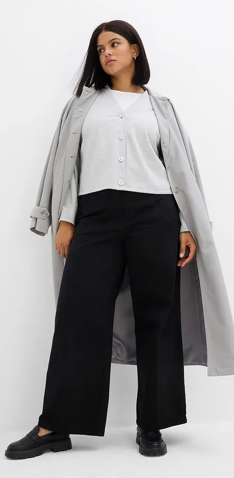 Cappotto grigio sopra camicetta bianca e pantaloni neri larghi. 