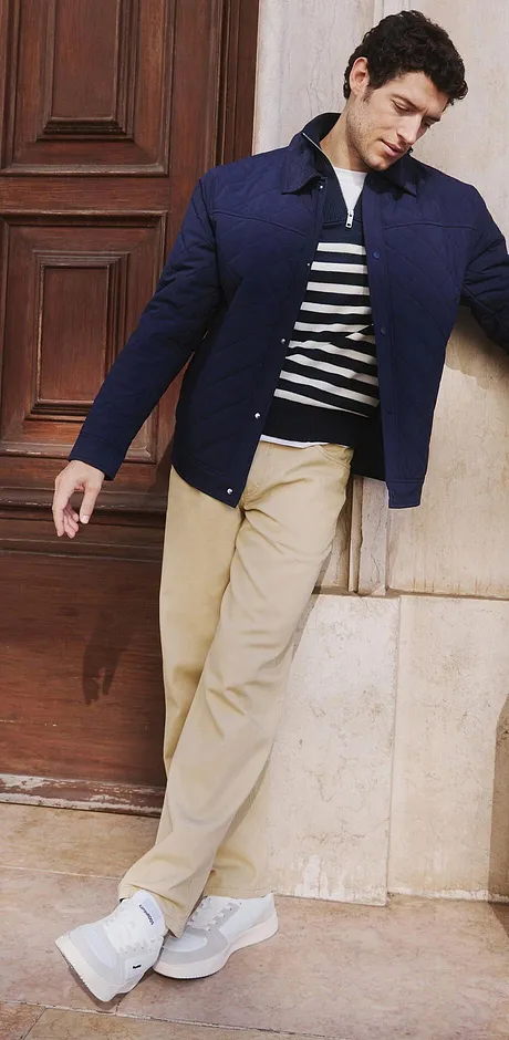 Una giacca blu scuro sopra un top a righe, pantaloni beige e sneakers bianche. 