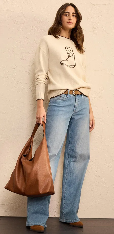 Maglione color crema con stampa di stivali, jeans larghi e grande borsa in pelle marrone. 