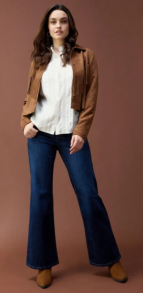 Giacca in pelle scamosciata sopra una blusa bianca, abbinata a jeans svasati. 