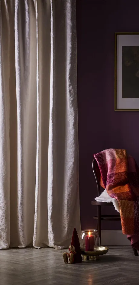 Tende chiare adornano la finestra. Una calda coperta è appoggiata su una sedia.