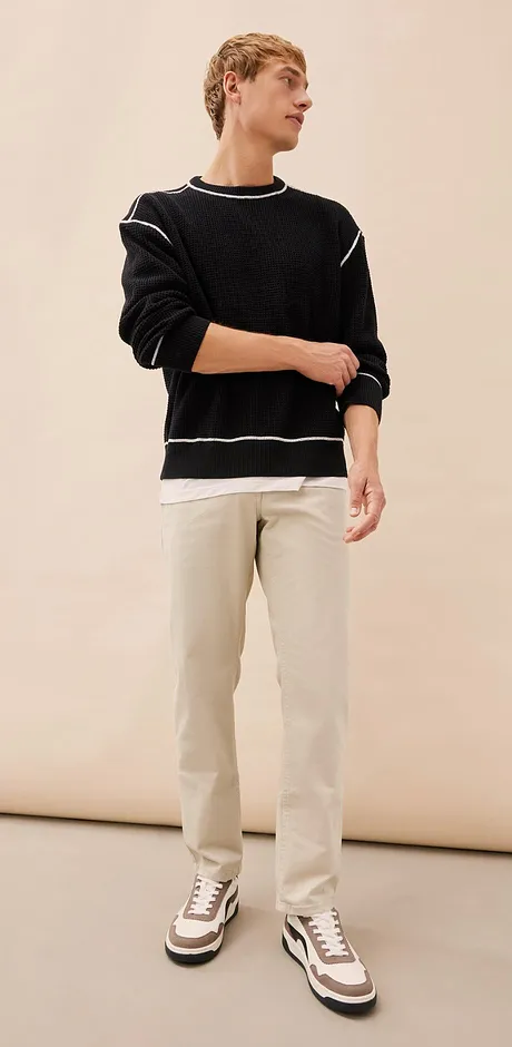 Look casual con maglione nero, pantaloni chiari e sneakers sportive.