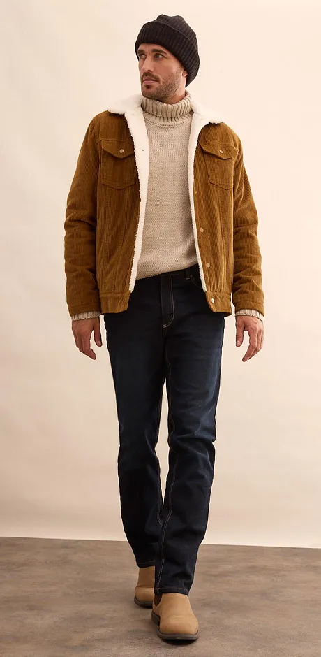 Giacca marrone, maglione a collo alto color crema e jeans scuri.