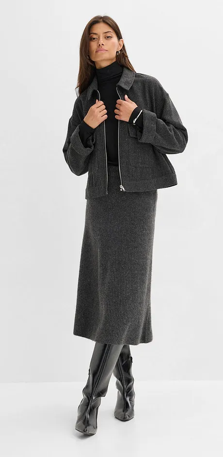 Gonna di lana grigia, maglione a collo alto nero, giacca corta e stivali di pelle al ginocchio.