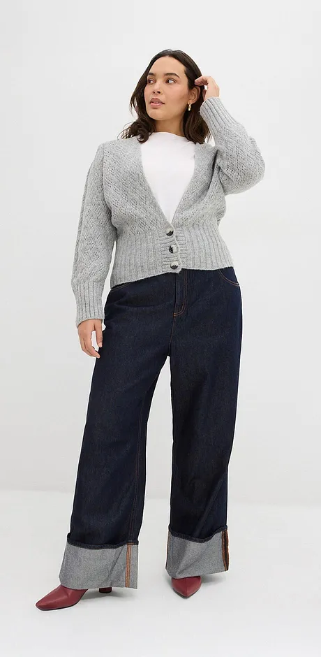 Cardigan grigio lavorato a maglia sopra un top bianco, jeans scuri con risvolto e scarpe rosse.