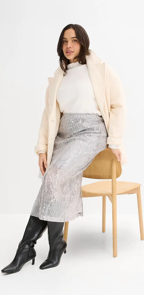 Cappotto color crema, maglione a collo alto bianco, gonna argentata e stivali di pelle neri.