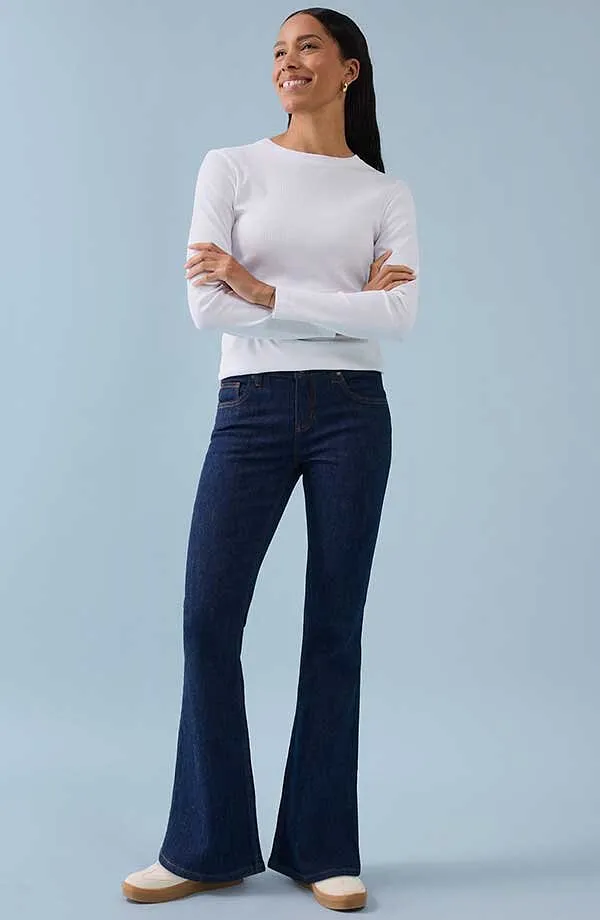 Maglia bianca a maniche lunghe abbinata a pantaloni a zampa blu scuro per un look elegante e senza tempo.