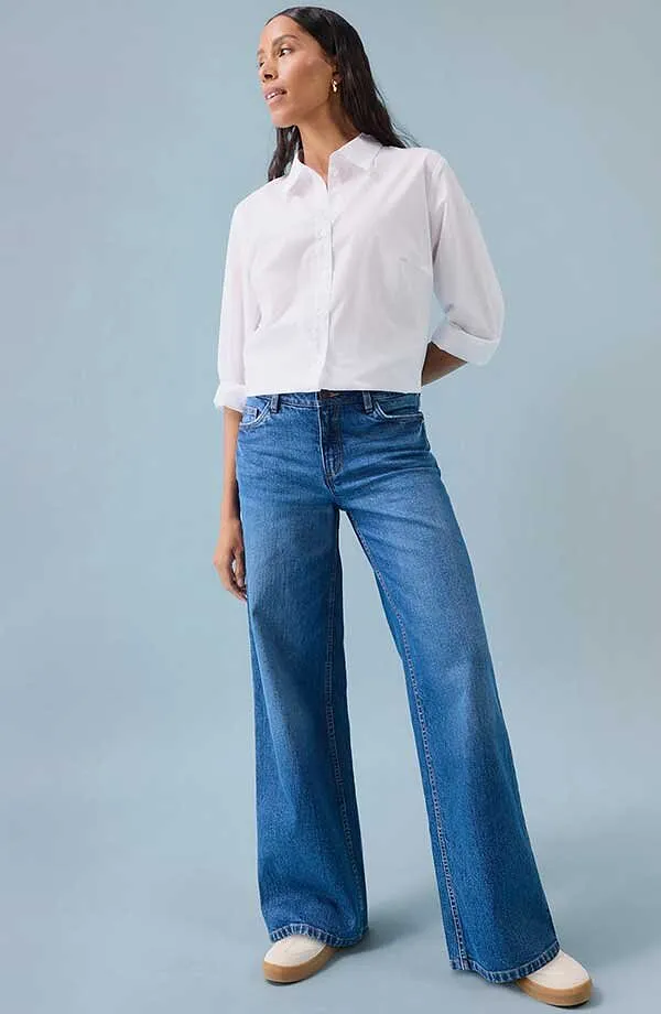 Camicia bianca con jeans blu a gamba larga e scarpe bianche.