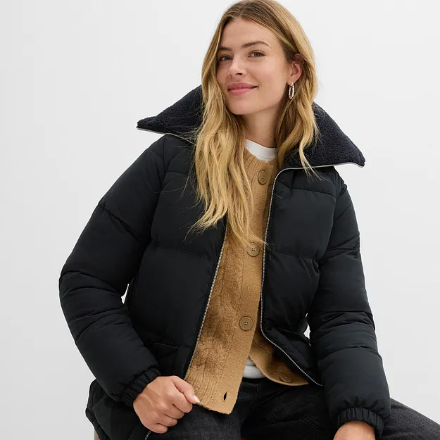 Giacca invernale nera con collo alto sopra un maglione giallo e una camicia bianca.