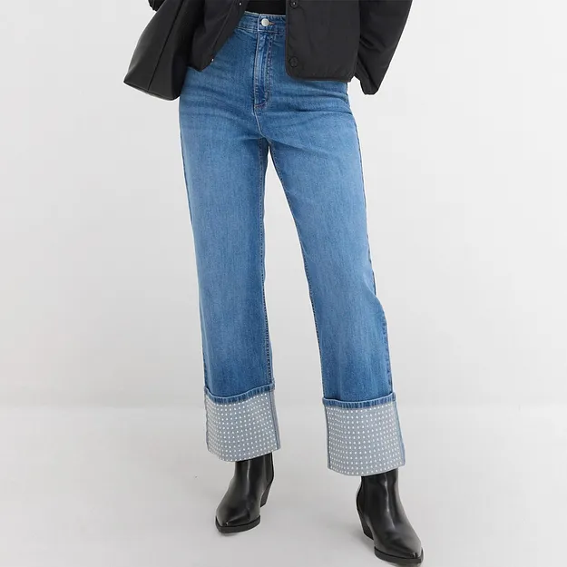Jeans blu con risvolto a quadri, stivali neri e blazer scuro abbinati.