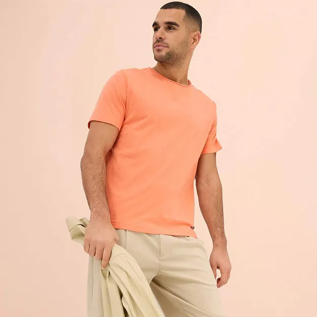 Maglietta color pesca abbinata a pantaloni chiari e un maglione coordinato come accessorio.