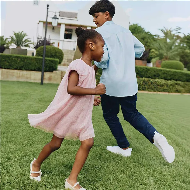 Una bambina con un vestito rosa balla allegramente in giardino.