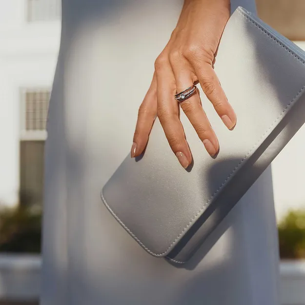 Abito bianco abbinato a una pochette chiara e a delicati anelli.