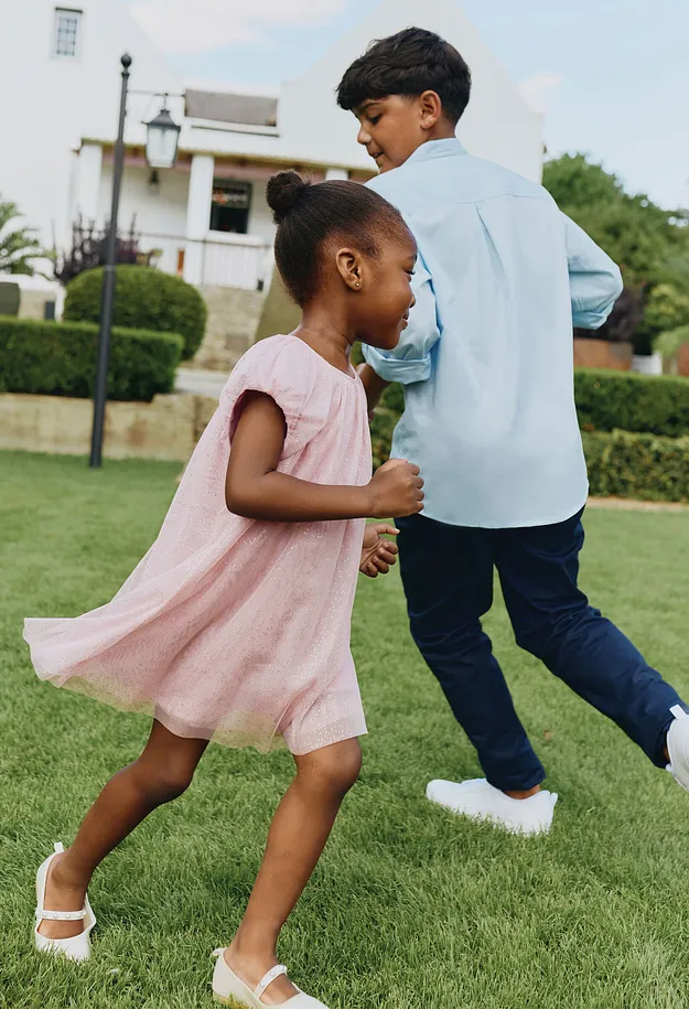 Una bambina con un vestito rosa balla allegramente in giardino.