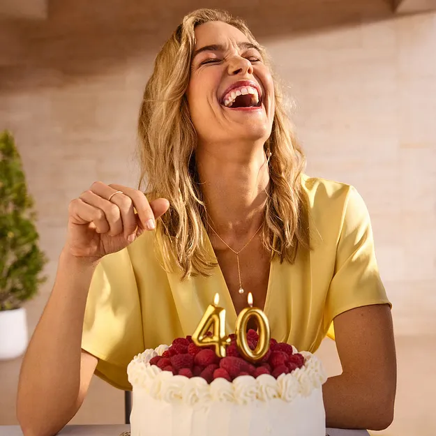 Donna con un abito giallo che festeggia il suo 40esimo compleanno con una torta e candeline a forma di 40.