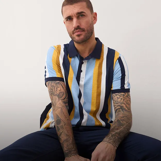 Polo a righe blu, gialle e bianche. Pantaloni scuri. 