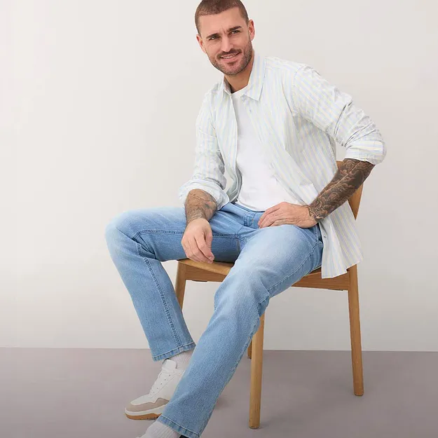 Camicia chiara a fantasia, jeans blu e sneaker bianche.