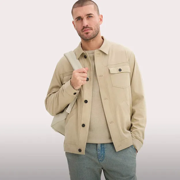 Giacca beige con bottoni e taschino sul petto sopra un maglione chiaro. Abbinata a jeans blu.