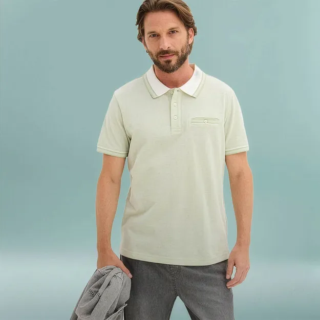 Un uomo indossa una polo verde chiaro con colletto bianco e pantaloni grigi.