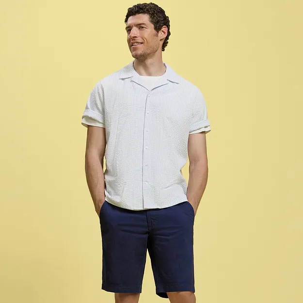 Un uomo indossa una camicia bianca a maniche corte e bermuda blu scuro.