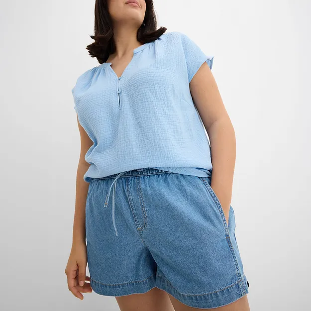 Top azzurro senza maniche con bottoni e shorts di jeans dal taglio morbido, per un look estivo disinvolto.