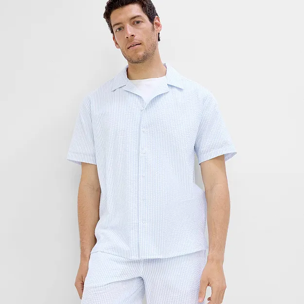 Un uomo indossa una camicia a maniche corte a righe azzurre e bianche con pantaloncini abbinati.