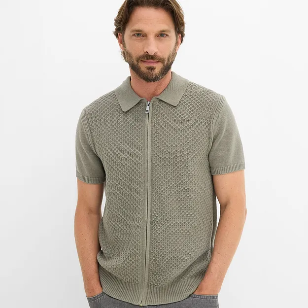 Polo verde lavorata a maglia con cerniera e motivo accattivante, abbinata a jeans scuri.