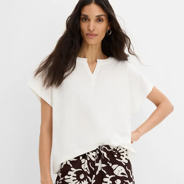 Blusa bianca leggera con scollo a V e pantaloni fantasia nei toni del marrone e del bianco.