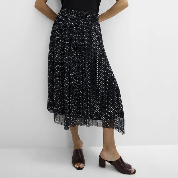 Un semplice top nero, una gonna plissettata a pois ed eleganti sandali marroni scuri.