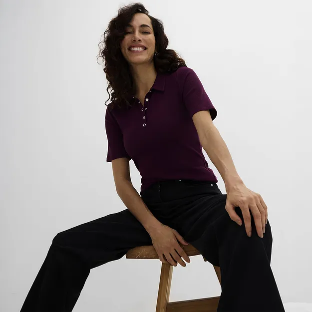 Una polo bordeaux con bottoni e un paio di pantaloni neri larghi.