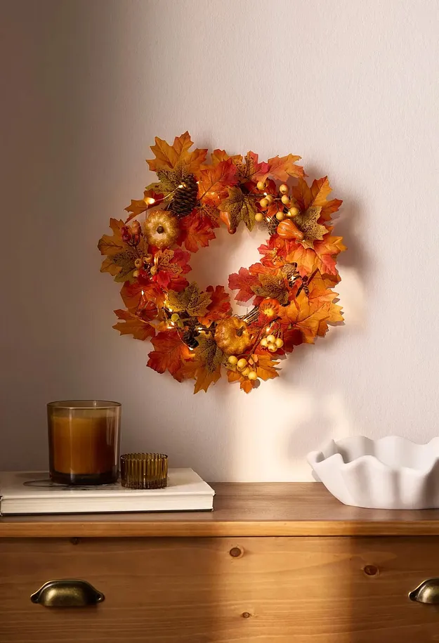 Una ghirlanda autunnale illuminata adorna la parete. La luce delle candele e una ciotola sul tavolo di legno.