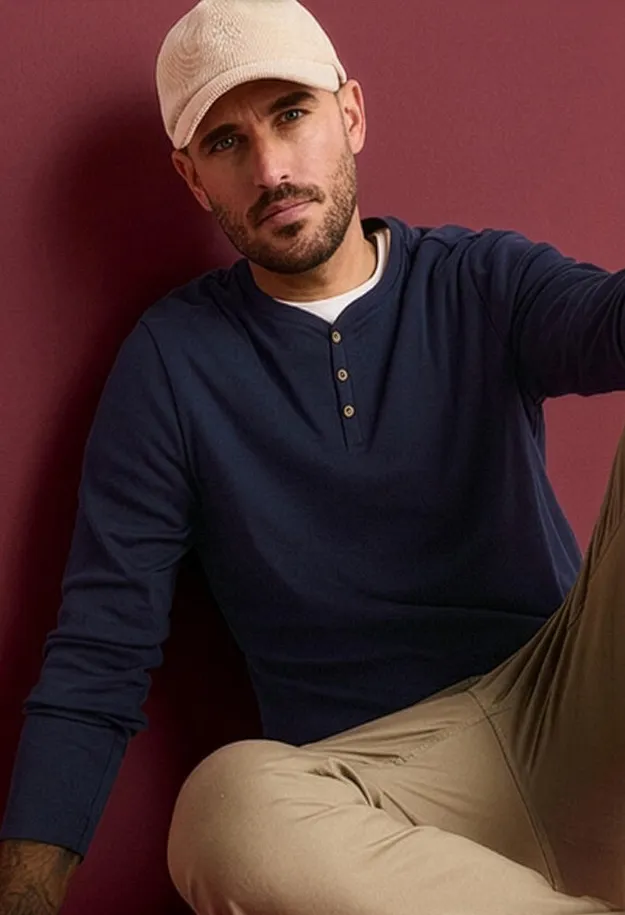 Un uomo indossa un berretto beige, una maglietta serafino blu navy e pantaloni beige.