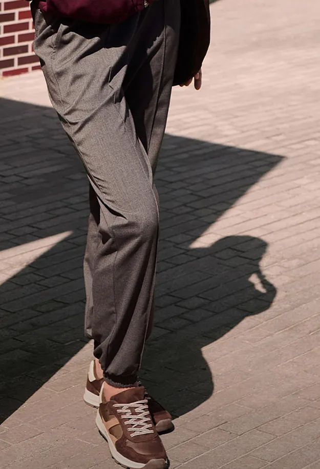 I pantaloni di tessuto grigio e le sneakers marroni definiscono questo look casual-elegante.