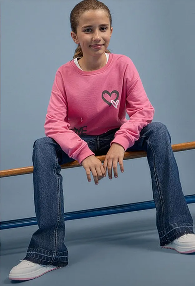 Outfit alla moda: maglietta rosa a maniche lunghe con un cuore, jeans larghi e comode sneakers bianche.