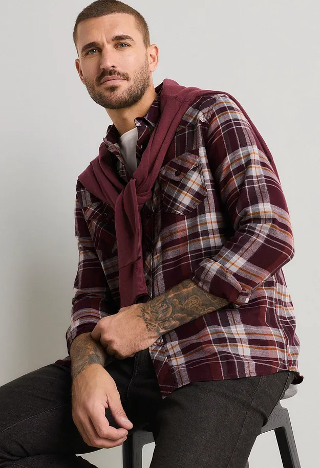 Camicia a quadri color bordeaux, jeans scuri e maglione abbinato.
