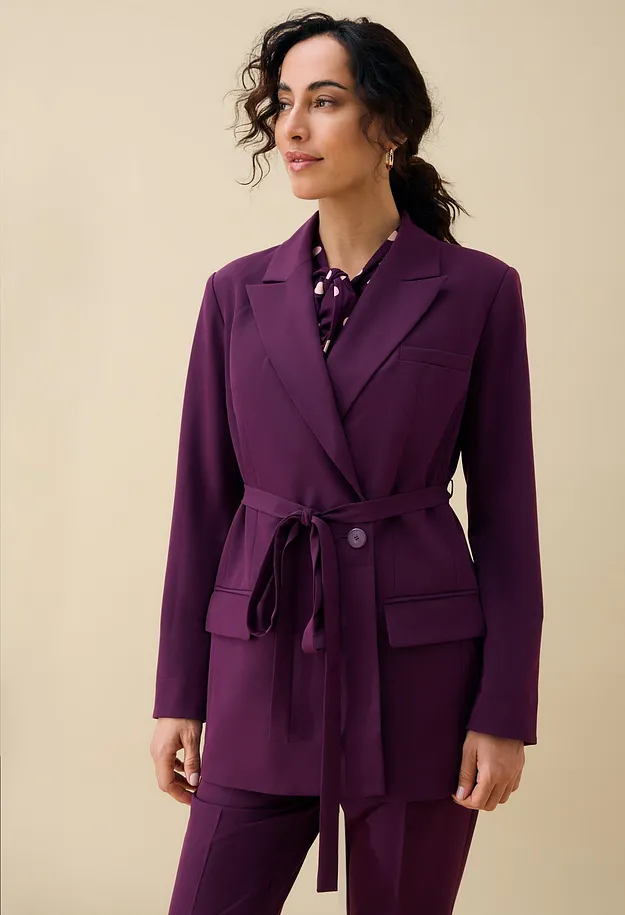 Elegante blazer viola con cintura e pantaloni abbinati, insieme a una camicetta a pois.