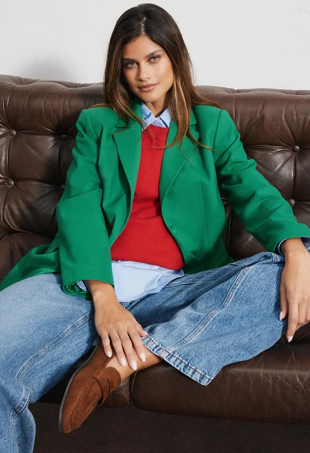 Blazer verde, maglietta rossa, camicia blu, jeans larghi e mocassini marroni.