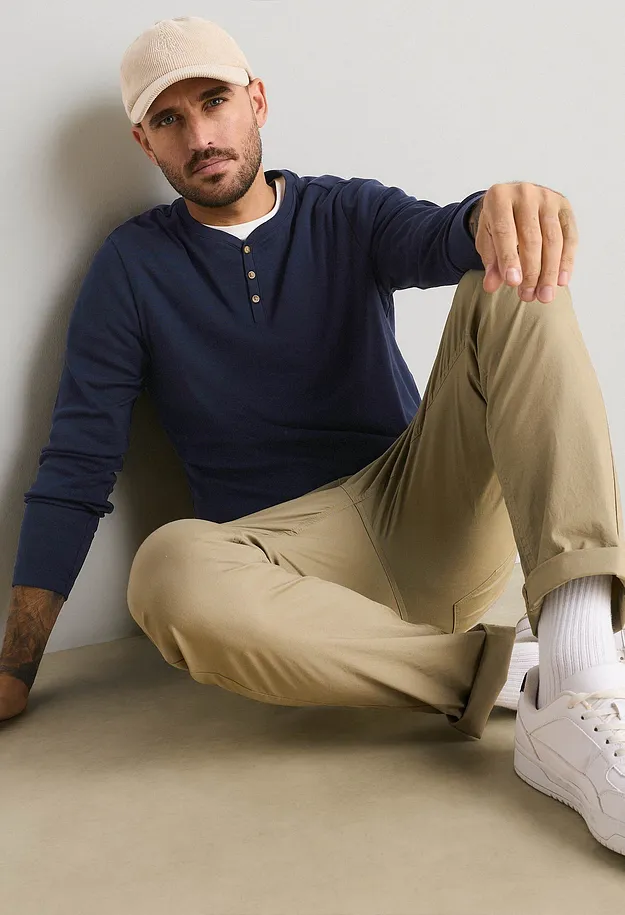 Cappellino beige, maglietta Henley blu, pantaloni beige e scarpe da ginnastica bianche.