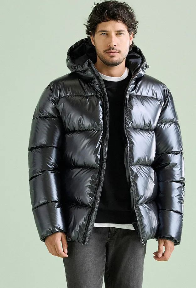 L'uomo indossa un'elegante giacca imbottita nera lucida con cappuccio e pantaloni scuri.