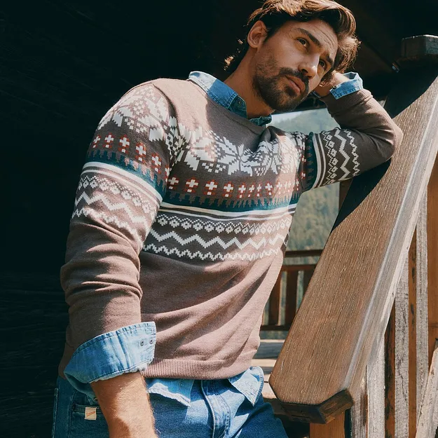 L'uomo indossa un maglione a fantasia sopra una camicia di jeans e dei jeans blu.