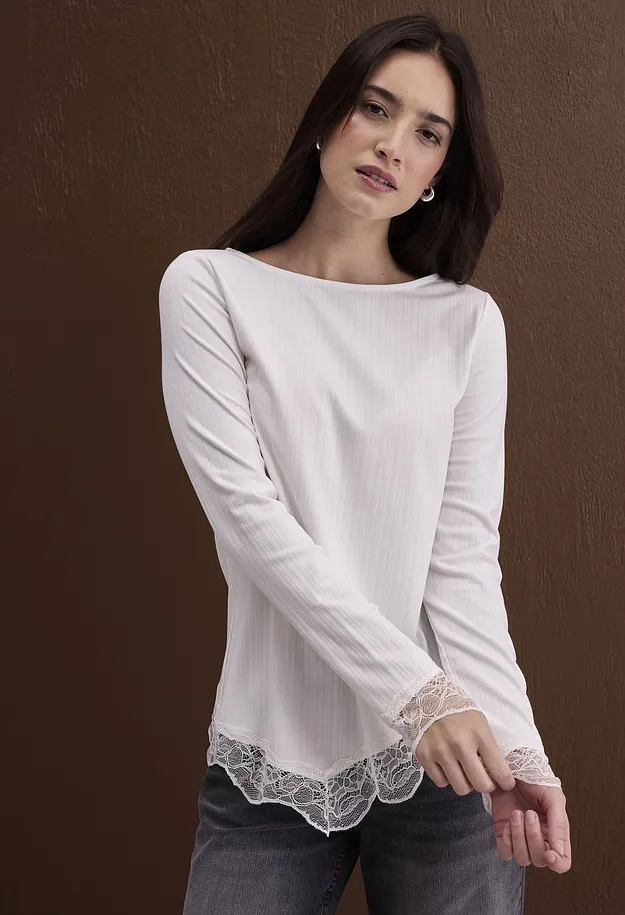 Elegante maglietta bianca a maniche lunghe con lavorazione a costine e pizzo, abbinata a jeans scuri.