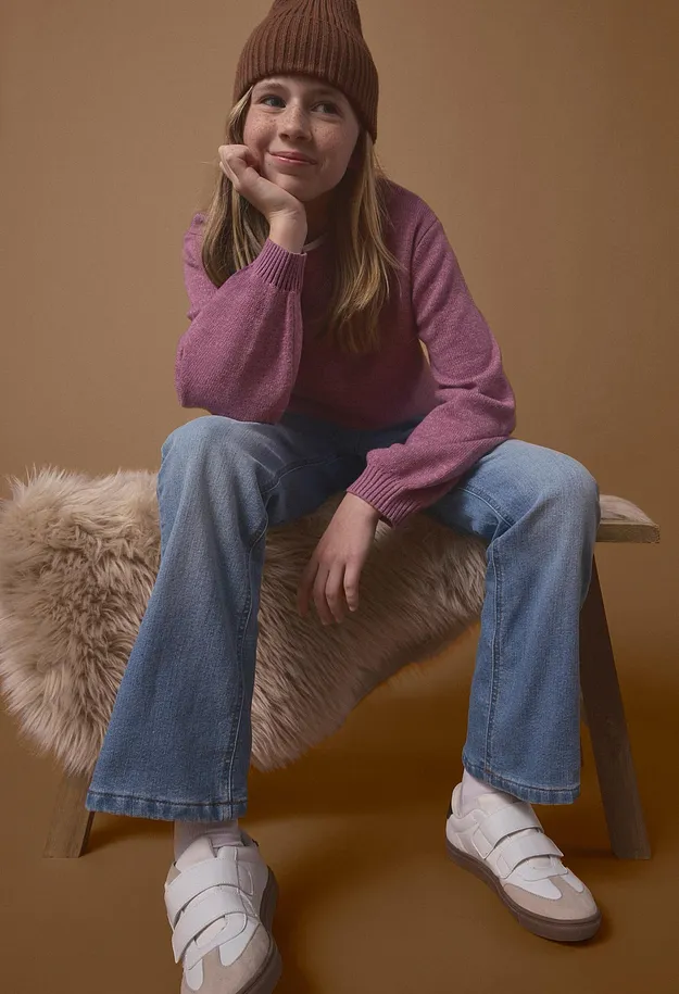 Berretto marrone, maglione rosa, jeans blu e scarpe da ginnastica bianche con chiusura a velcro.
